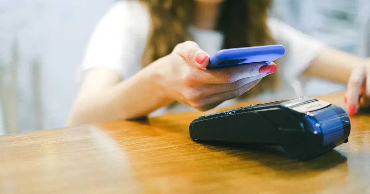 Mulher aproxima smartphone de terminal de pagamento.