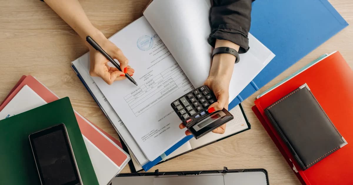 Profissional confere documentos financeiros com calculadora.
